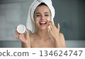 Excited young woman looking at camera advertizing cosmetic face cream 134624747