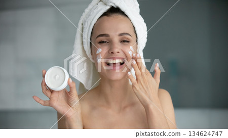 Excited young woman looking at camera advertizing cosmetic face cream 134624747