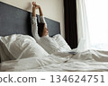 Awakened smiling young lady stretching arms on bed holding notebook 134624751