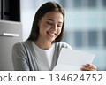Cheerful young woman employee reading paper document received in letter 134624752