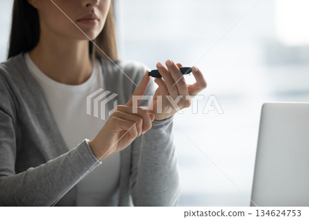 Closeup young lady pricking finger with digital glucometer by computer 134624753