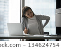 Exhausted young businesswoman suffering from back pain at work desk 134624754
