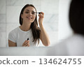 Beautiful smiling young woman applying mascara on eyelashes by mirror 134624755