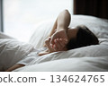 Young woman lying in bed hiding closed eyes beneath arm 134624765
