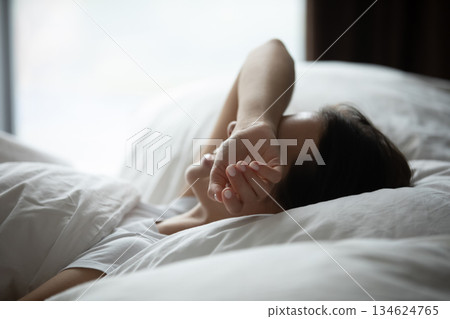 Young woman lying in bed hiding closed eyes beneath arm Young woman lying in bed hiding closed eyes beneath arm 134624765