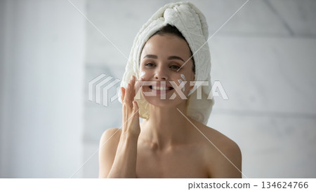 Headshot portrait cheerful young woman applying cosmetic cream on face 134624766