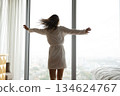 Carefree millennial woman spinning around in bedroom with picture window 134624767