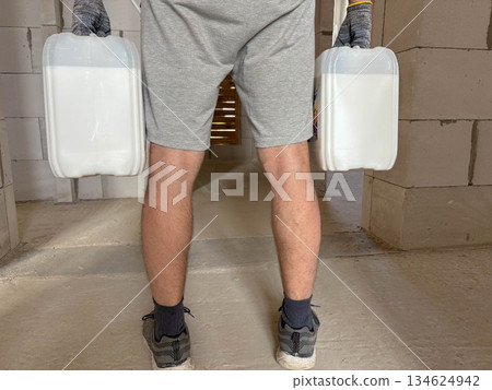 A man at a construction site holds a heavy canister of wall priming solution. A man at a construction site holds a heavy canister of wall priming solution. 134624942