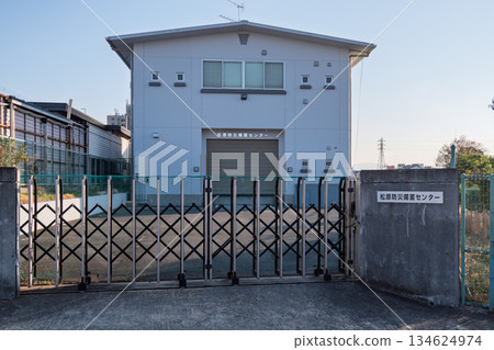 大阪府松原市災害防備物資儲存中心全景：一座建於 20 世紀 80 年代的倉庫和為應對洪水和地震而準備的藍色網狀大門。 134624974