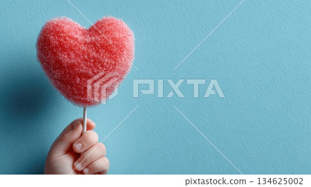 A child's hand holding a red cotton candy heart on a stick on a blue background in honor of Valentine's Day or Mother's Day A child's hand holding a red cotton candy heart on a stick on a blue background in honor of Valentine's Day or Mother's Day 134625002