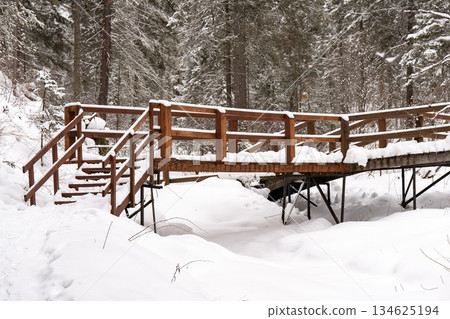 Wooden bridge over river covered with snow in forest in winter. Wooden bridge over river covered with snow in forest in winter. 134625194