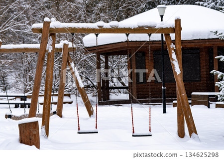Wooden children's swing house in the park in winter under the snow. 134625298