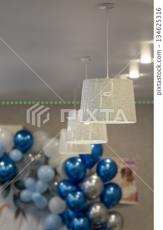 Lamps with white shades hang from the ceiling against a backdrop of balloons. 134625316