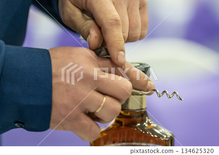 A man with a corkscrew in his hands opens a bottle of brandy. A man with a corkscrew in his hands opens a bottle of brandy. 134625320