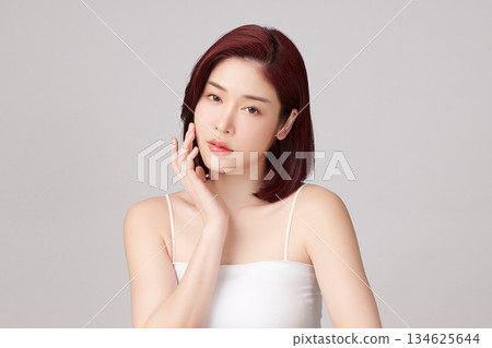 A beautiful young Asian woman with clean, fresh skin against a grey background. Skincare, facial treatment, cosmetology, beauty, and spa. An elegant portrait of an Asian woman. 134625644