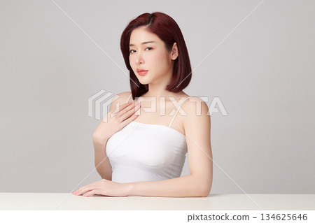 A beautiful young Asian woman with clean, fresh skin against a grey background. Skincare, facial treatment, cosmetology, beauty, and spa. An elegant portrait of an Asian woman. 134625646