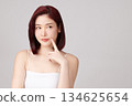 A beautiful young Asian woman with clean, fresh skin against a grey background. Skincare, facial treatment, cosmetology, beauty, and spa. An elegant portrait of an Asian woman. 134625654