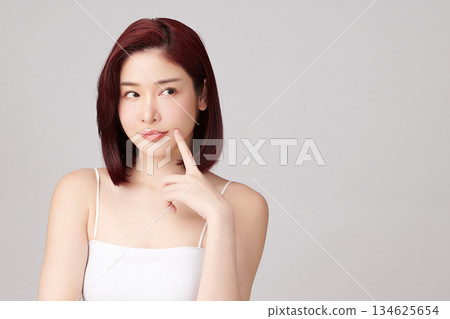 A beautiful young Asian woman with clean, fresh skin against a grey background. Skincare, facial treatment, cosmetology, beauty, and spa. An elegant portrait of an Asian woman. 134625654