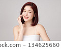 A beautiful young Asian woman with clean, fresh skin against a grey background. Skincare, facial treatment, cosmetology, beauty, and spa. An elegant portrait of an Asian woman. 134625660