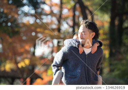 秋葉飄落的公園裡，笑容滿面的父母和孩子們互相肩扛著。這是展現父子共度假期溫馨家庭生活的畫面。 134626919