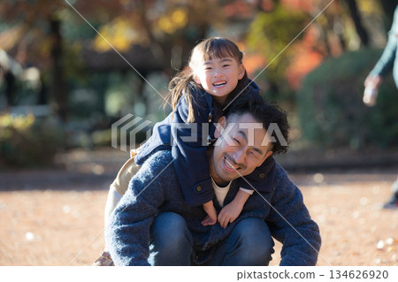 Smiling parents and children doing shoulder-carrying in a park with autumn leaves. A lifestyle image of a father and son spending a holiday together as a family. 134626920
