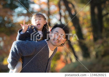 Smiling parents and children doing shoulder-carrying in a park with autumn leaves. A lifestyle image of a father and son spending a holiday together as a family. 134626921