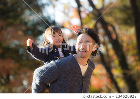 Smiling parents and children doing shoulder-carrying in a park with autumn leaves. A lifestyle image of a father and son spending a holiday together as a family. 134626922