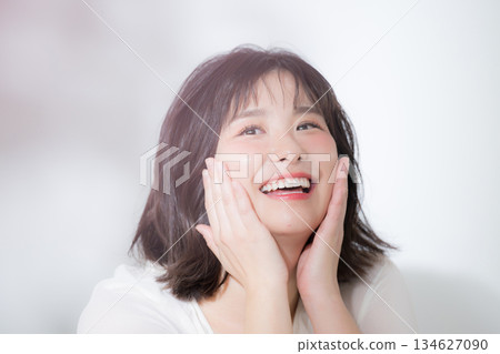 A close-up beauty image of a young, soothing woman with a clear, happy look, smiling and holding her hand on her cheek 134627090