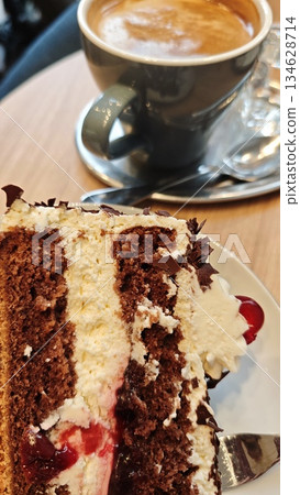 Slice of chocolate cake with cream and berry filling served on a plate with a cup of coffee in a cafe setting. The image represents indulgence, dessert enjoyment, and cozy coffee break moment Slice of chocolate cake with cream and berry filling served on a plate with a cup of coffee in a cafe setting. The image represents indulgence, dessert enjoyment, and cozy coffee break moment 134628714