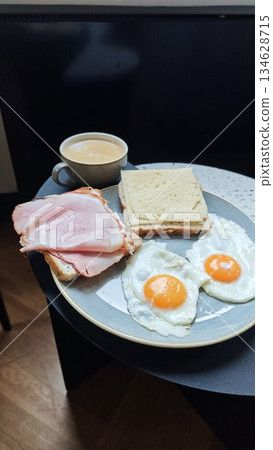 Plate with fried egg ham cheese sandwich and coffee served on a small table in a cozy cafe setting. The image represents classic breakfast routine, comfort food, and relaxed morning lifestyle 134628715