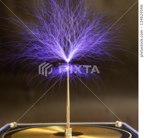 Streams of violet plasma discharge from the top of a Tesla coil in a high-voltage experiment 134629566