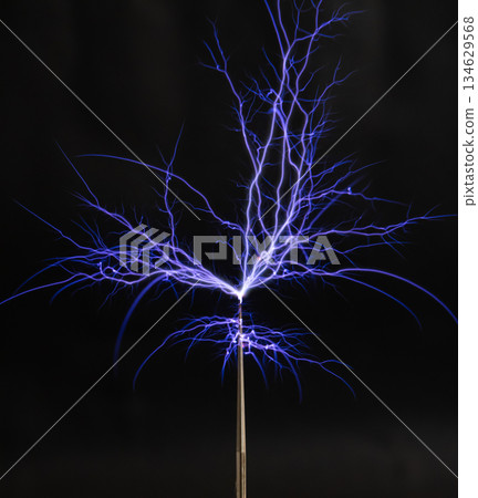 Streams of violet plasma discharge from the top of a Tesla coil in a high-voltage experiment 134629568