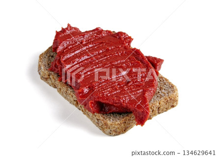 thick red tomato paste spread thickly on a piece of coarse black bread. thick red tomato paste spread thickly on a piece of coarse black bread. 134629641