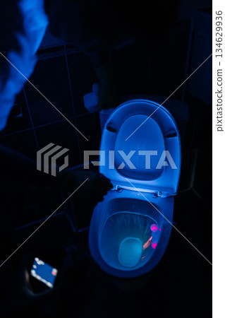 Vertical shot of toilet bowl illuminating under ultraviolet light, revealing hidden traces of dirt, bacteria and germs, highlighting need for deep hygiene and effective bathroom cleaning, nobody. 134629936