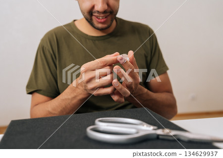 Close-up of person cutting adhesive medical bandage with pair of scissors, carefully applying first aid to bandaged finger, showing self-care for minor injury or wound. 134629937