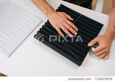 High-angle view of man checking soundproof foam panel doing quality check before installing acoustic insulation, preparing for diy project to improve audio quality and reduce noise for home recording. High-angle view of man checking soundproof foam panel doing quality check before installing acoustic insulation, preparing for diy project to improve audio quality and reduce noise for home recording. 134629956