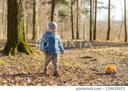 Happy baby child outdoor. Little toddler boy with toy car having fun on walk in park. Baby son smiling playing outdoor. Little child resting walking in nature. Little toddler child having fun on walk 134630973