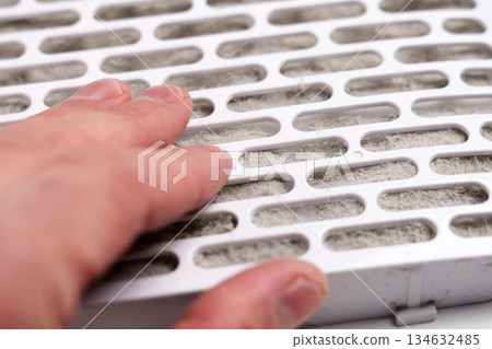 Air filter element clogged with dust fibers touched by a human hand. Used filtration cartridge 134632485