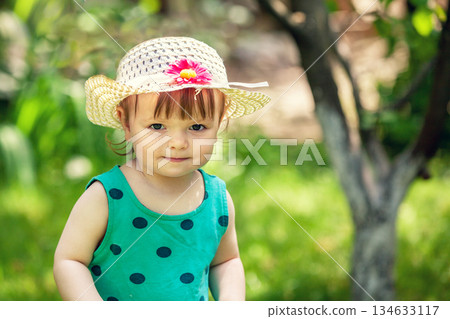 Happy baby girl in a straw hat sits in the summer garden Happy baby girl in a straw hat sits in the summer garden 134633117