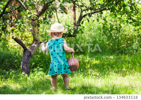 Happy baby girl in a straw hat sits in the summer garden Happy baby girl in a straw hat sits in the summer garden 134633118