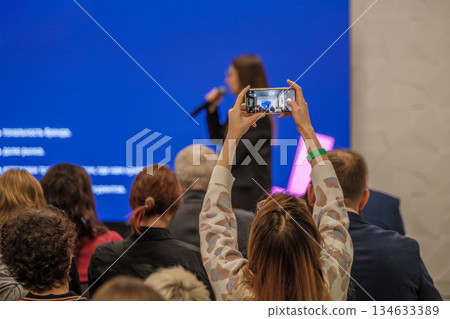 Audience at conference captures speaker on stage using a smartphone during presentation 134633389