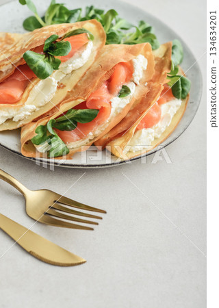 Crepes or thin pancakes with lightly salted salmon, soft cheese and cornsalad Crepes or thin pancakes with lightly salted salmon, soft cheese and cornsalad 134634201