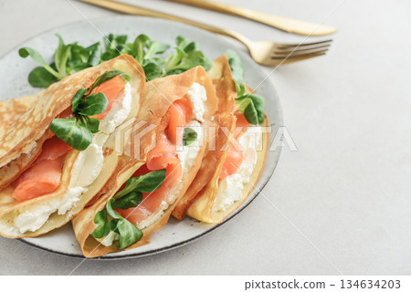 Crepes or thin pancakes with lightly salted salmon, soft cheese and cornsalad 134634203