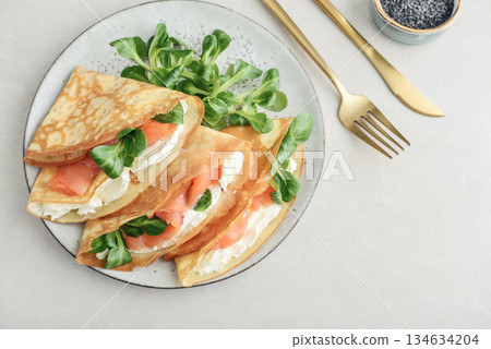 Crepes or thin pancakes with lightly salted salmon, soft cheese and cornsalad 134634204