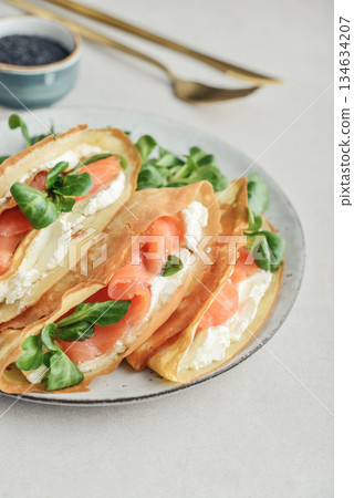 Crepes or thin pancakes with lightly salted salmon, soft cheese and cornsalad 134634207