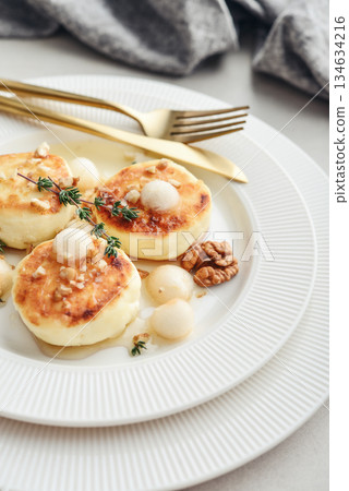 cottage cheese pancakes, syrniki, curd fritters served with pear balls, walnut and honey 134634216