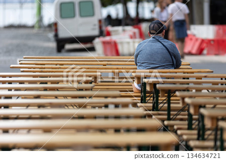 Person sitting alone on wooden bench during outdoor event Person sitting alone on wooden bench during outdoor event 134634721