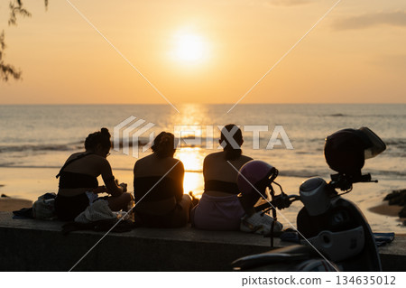 Sea sunset on the coast of Thailand. Women watch sunset on beach while sitting near the shore and enjoying the view of the ocean during evening hours with motorbike parked nearby. High quality photo Sea sunset on the coast of Thailand. Women watch sunset on beach while sitting near the shore and enjoying the view of the ocean during evening hours with motorbike parked nearby. High quality photo 134635012