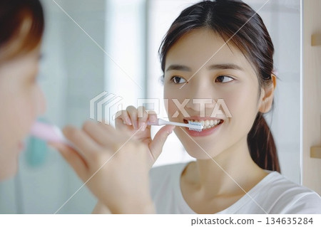 Young woman holding a toothbrush and smiling with white teeth in a bright bathroom Young woman holding a toothbrush and smiling with white teeth in a bright bathroom 134635284