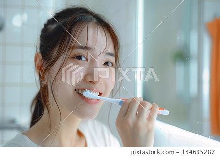 一位年輕女子在明亮的浴室裡拿著牙刷，露出潔白的牙齒，笑容燦爛。 134635287
